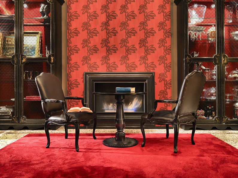 Sedie e tavolo in legno scuro, camino scuro in ambiente rosso. Interior design per hotel di lusso, a cura di Bertelè Mobili