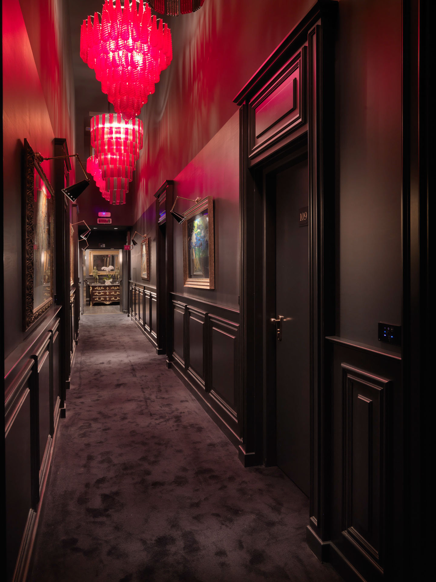 Corridoio hotel di lusso, boiserie e tappeto nero, lampadari sospesi rossi. Interior design hospitality di Bertelè Mobili (Verona)