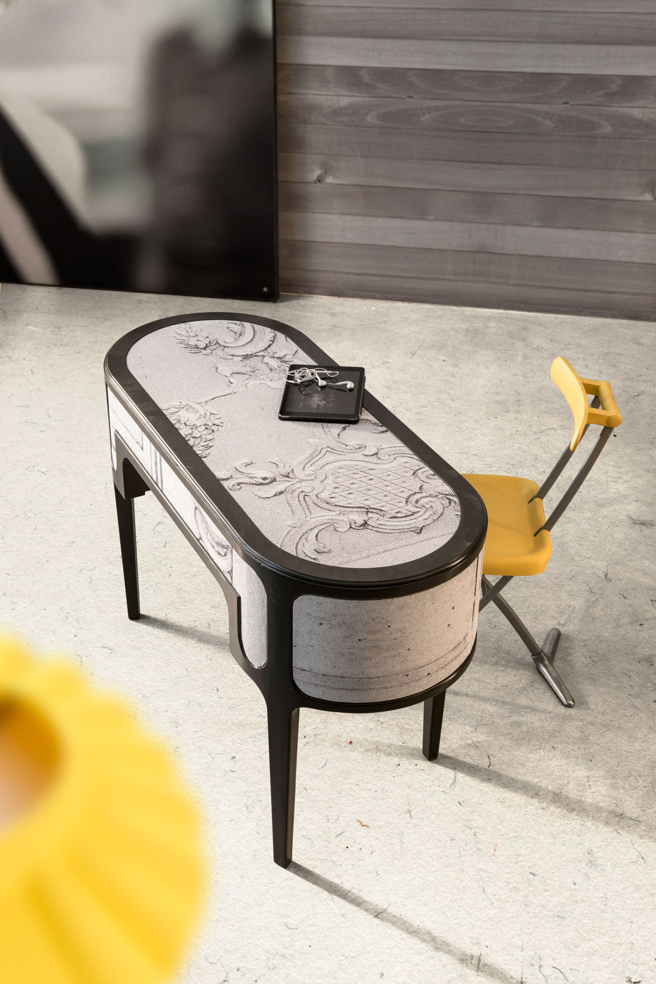 Scrivania sagomata nera con piano decorato da motivi classici a rilievo, laptop e sedia gialla moderna in uno studio minimalista. Progetto a cura di Bertelè Mobili (Verona)