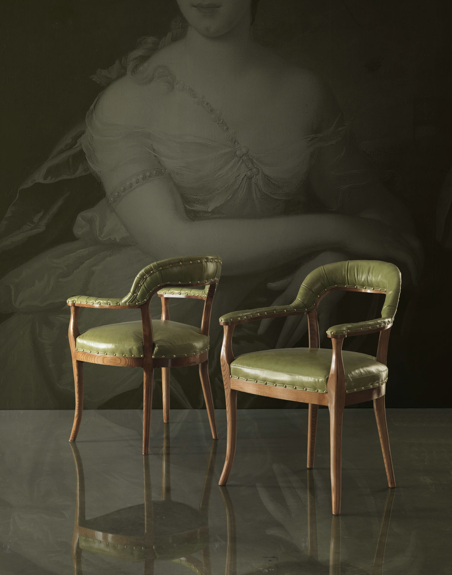 Coppia di poltroncine classiche in pelle verde con schienale curvo e borchie dorate su sfondo con ritratto d'epoca. Progetto Bertelè Mobili