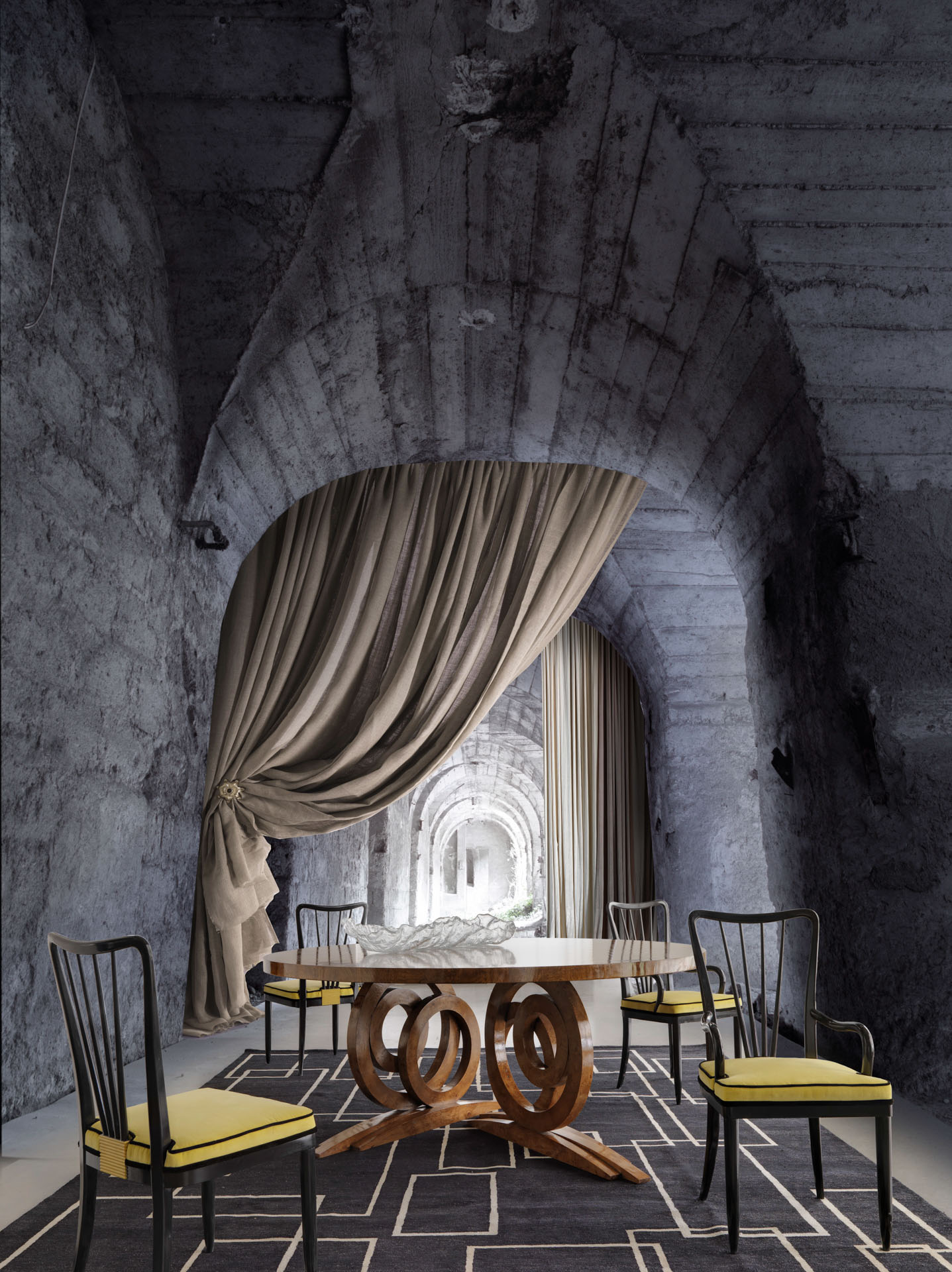 Sala da pranzo di lusso con tavolo tondo in legno dalla base scultorea a cerchi, sedie nere con seduta gialla e ambiente scenografico. Interior design profettato da Bertelè Mobili. 